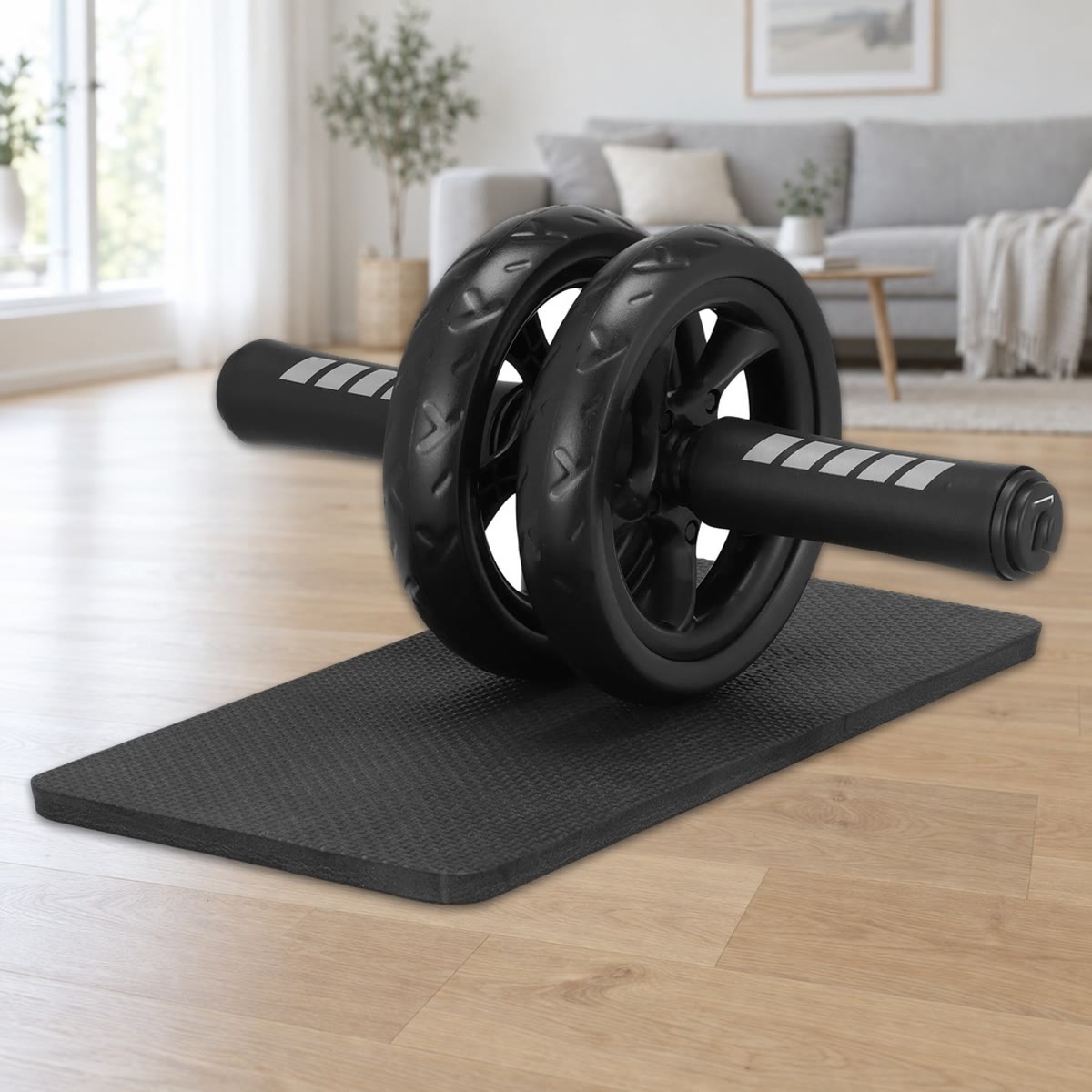 Ab wheel med to hjul på 15 cm og skumhåndtag, placeret på den sorte knæmåtte på et lyst parketgulv