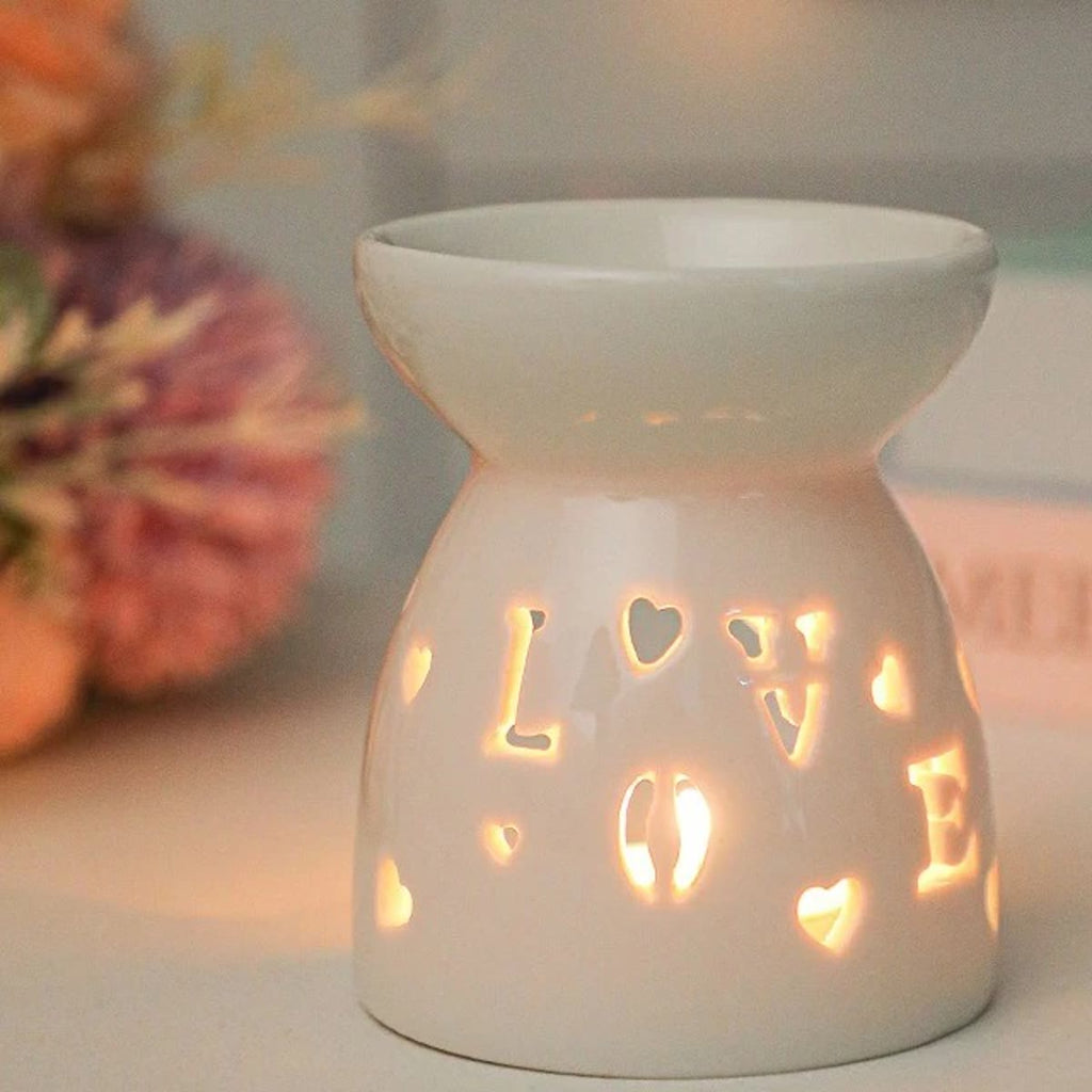 Duftlampe i hvid keramik med LOVE og små hjerter skåret ud, tændt med et fyrfadslys