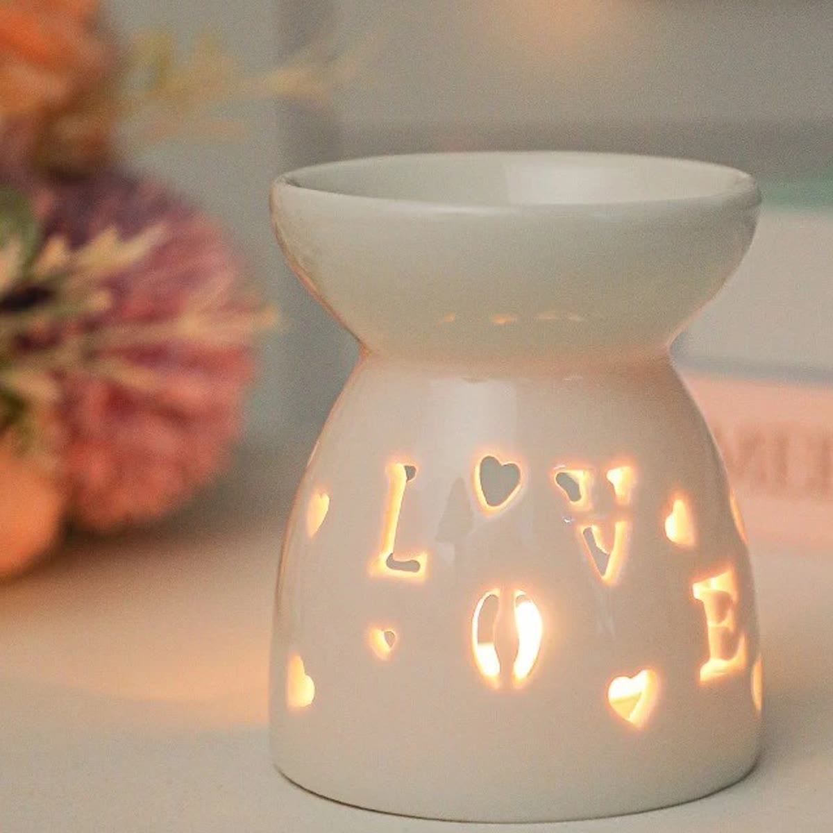 Duftlampe i hvid keramik med LOVE og små hjerter skåret ud, tændt med et fyrfadslys
