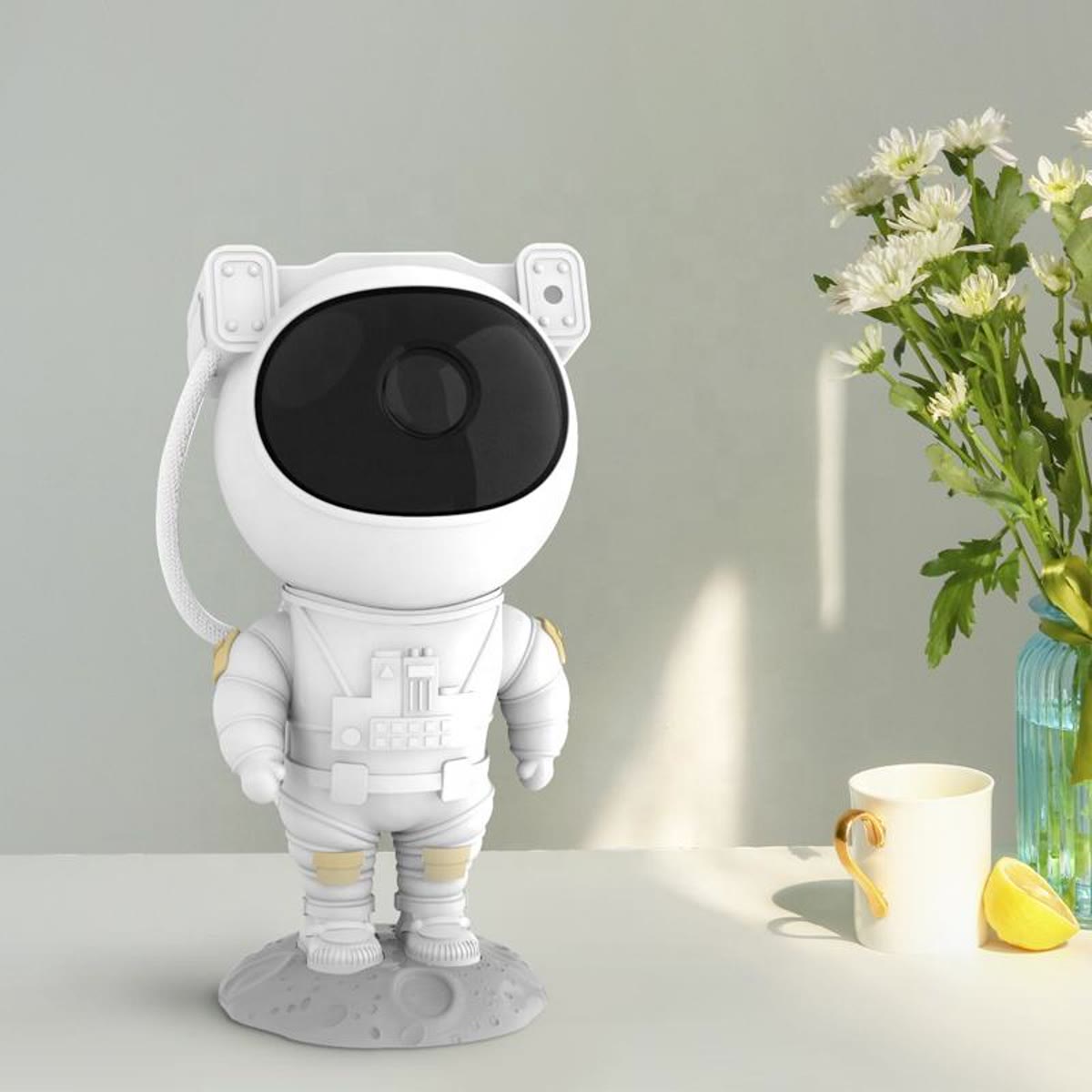 Hvid astronaut projektor på et bord ved et vindue med en vase med blomster bagved
