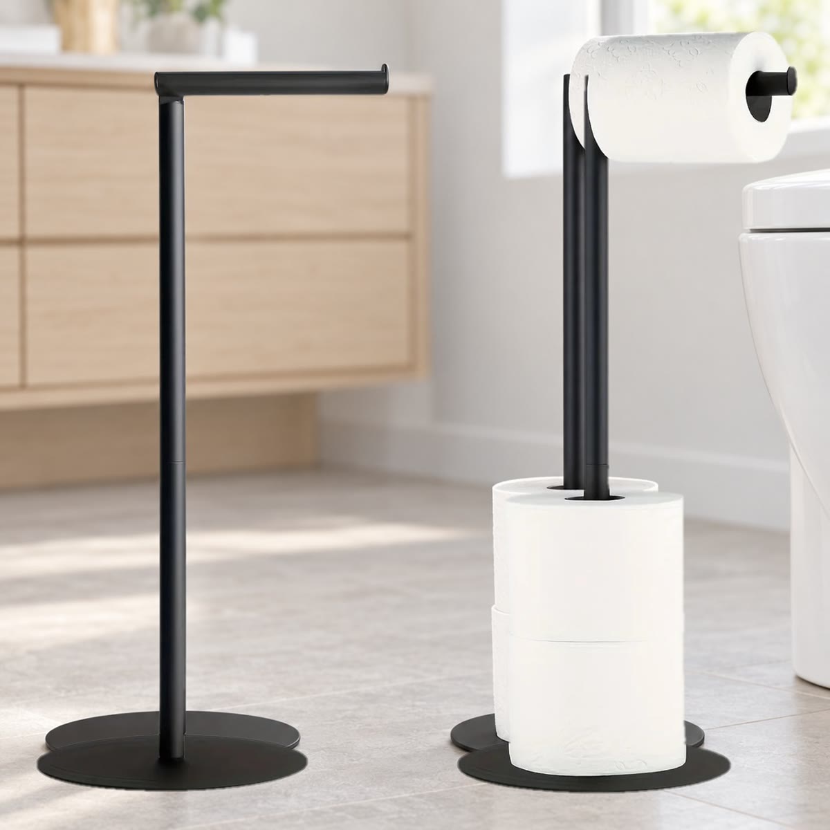 Fritstående toiletrulleholder i sort stål på et badeværelsesgulv, vist tom og med rulle på toppen og reserveruller på stangen