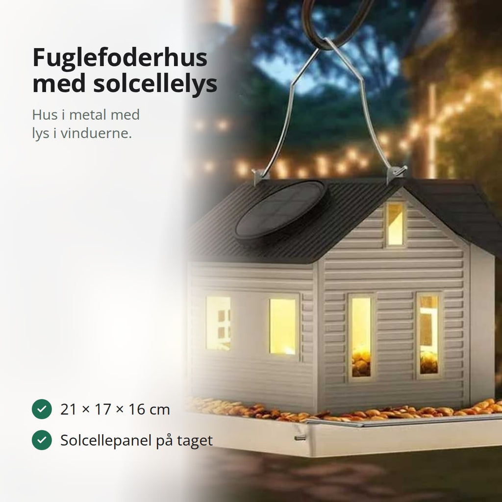 Fuglefoderhus formet som et hvidt hus i metal med sort tag, solcellepanel og foderbræt
