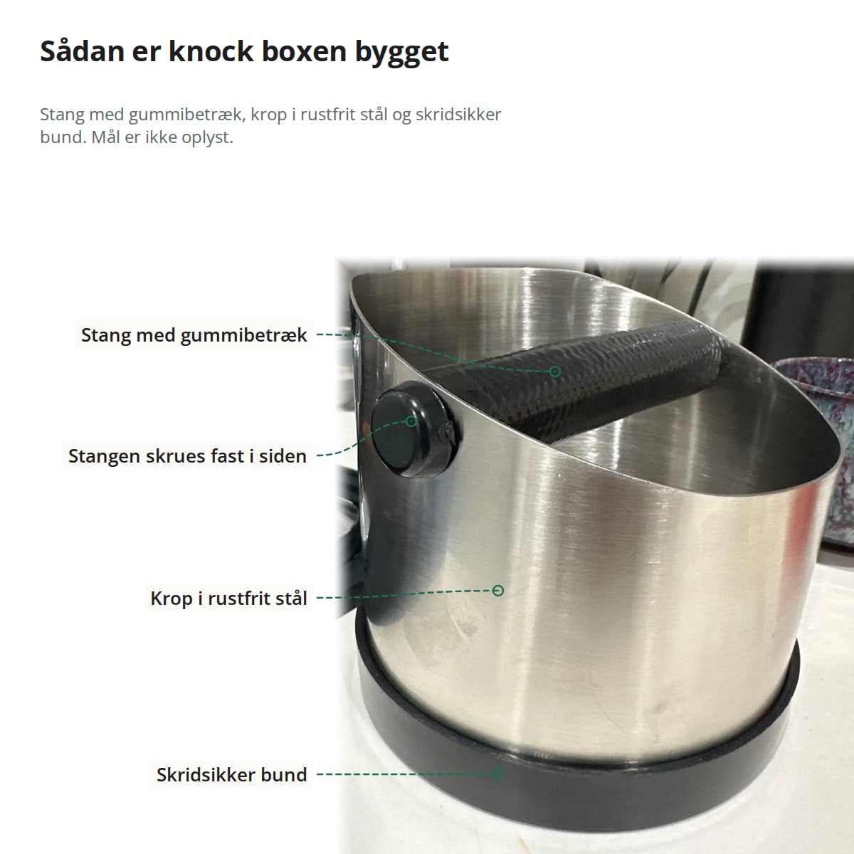 Knock boxen set fra siden med markeringer: stangen med gummibetræk, der skrues fast i siden, kroppen i rustfrit stål og den skridsikre bund; mål er ikke oplyst