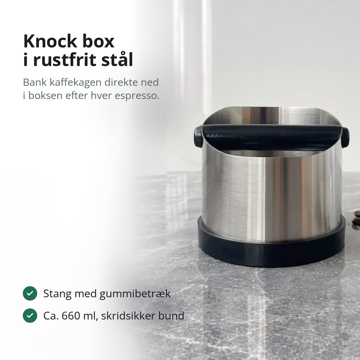 Knock box i rustfrit stål med sort bankestang og sort bund på en grå marmorbordplade, med teksten: knock box i rustfrit stål, bank kaffekagen direkte ned i boksen efter hver espresso; stang med gummibetræk, ca. 660 ml, skridsikker bund