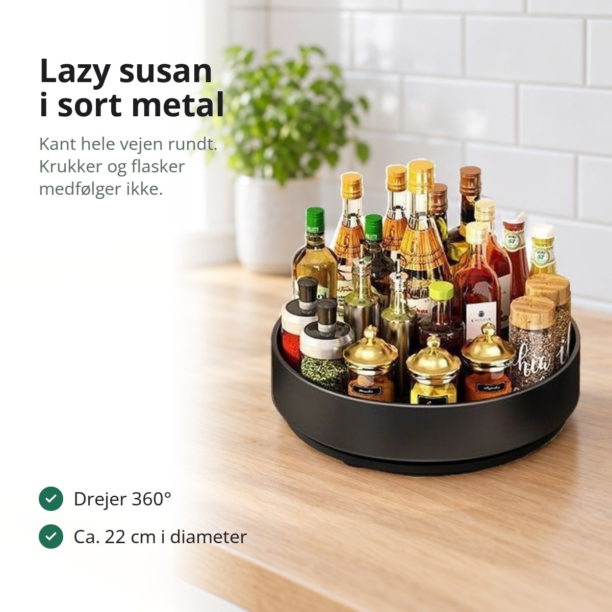 Lazy susan i sort metal med krydderiglas og olie- og eddikeflasker på et lyst køkkenbord i eg, med teksten: lazy susan i sort metal, kant hele vejen rundt, krukker og flasker medfølger ikke; drejer 360°, ca. 22 cm i diameter