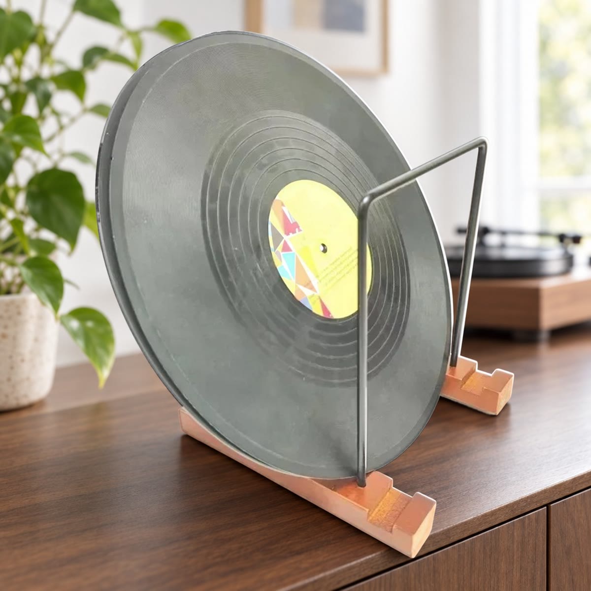 Vinylplade, der står i en pladeholder med fødder i træ og rammer i sort metal, på en skænk i valnød