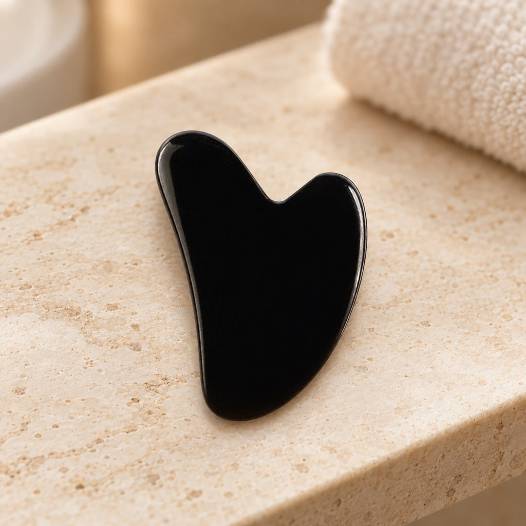 Hjerteformet gua sha i sort obsidian på en travertinhylde på badeværelset