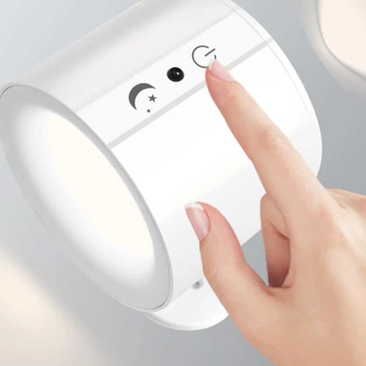 Hvid væglampe, hvor en finger trykker på touchknappen på siden