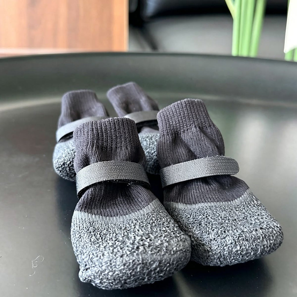 Fire grå og sorte hundesokker med gummisål og velcro på et mørkt bord