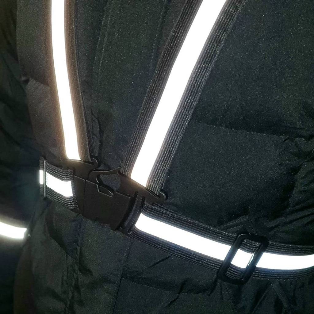 Refleksvesten spændt uden på en mørk vinterjakke, med spændet synligt
