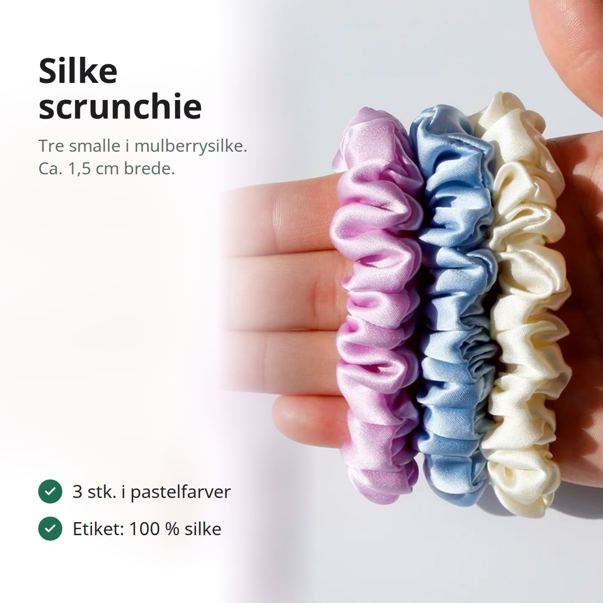 Tre smalle silke scrunchies i rosa-lilla, lyseblå og creme i en åben hånd, med teksten: tre smalle i mulberrysilke, ca. 1,5 cm brede, 3 stk. i pastelfarver, etiket: 100 % silke