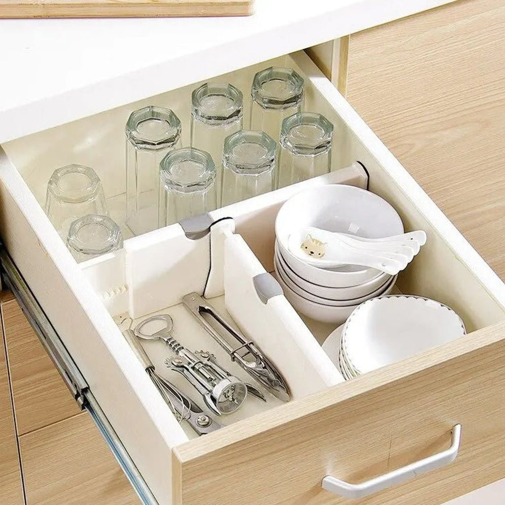 Køkkenskuffe inddelt med hvide skuffeinddelere, med glas, skåle og redskaber i hvert sit rum