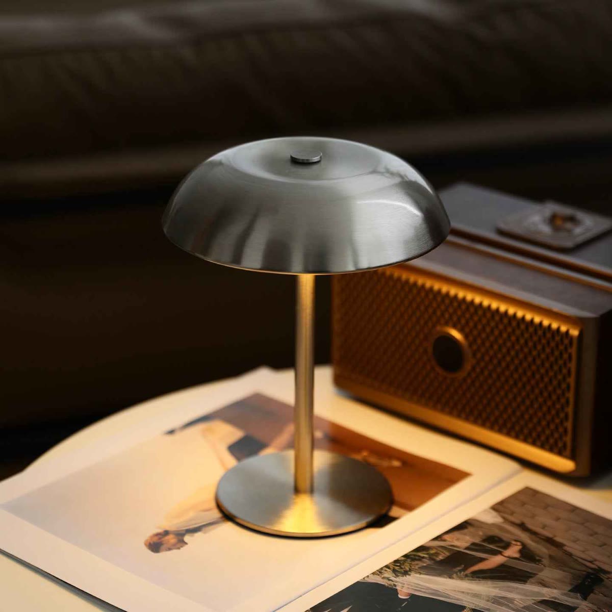 Mushroom lampe i børstet metal tændt på et bord ved siden af en gammel radio og gamle fotografier