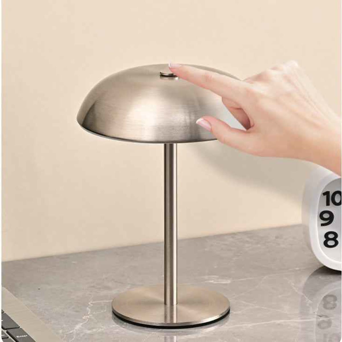 En hånd, der trykker på touch-sensoren på toppen af lampen, på et marmorbord