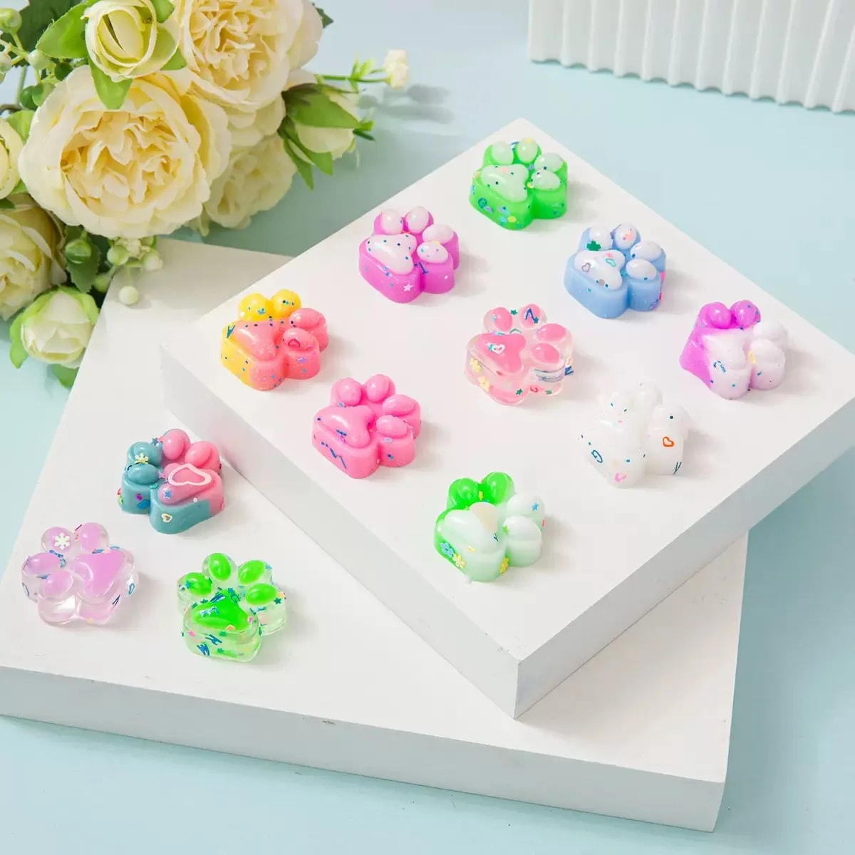 Squishy-kattepoter i pastelfarver på et hvidt podie med blomster