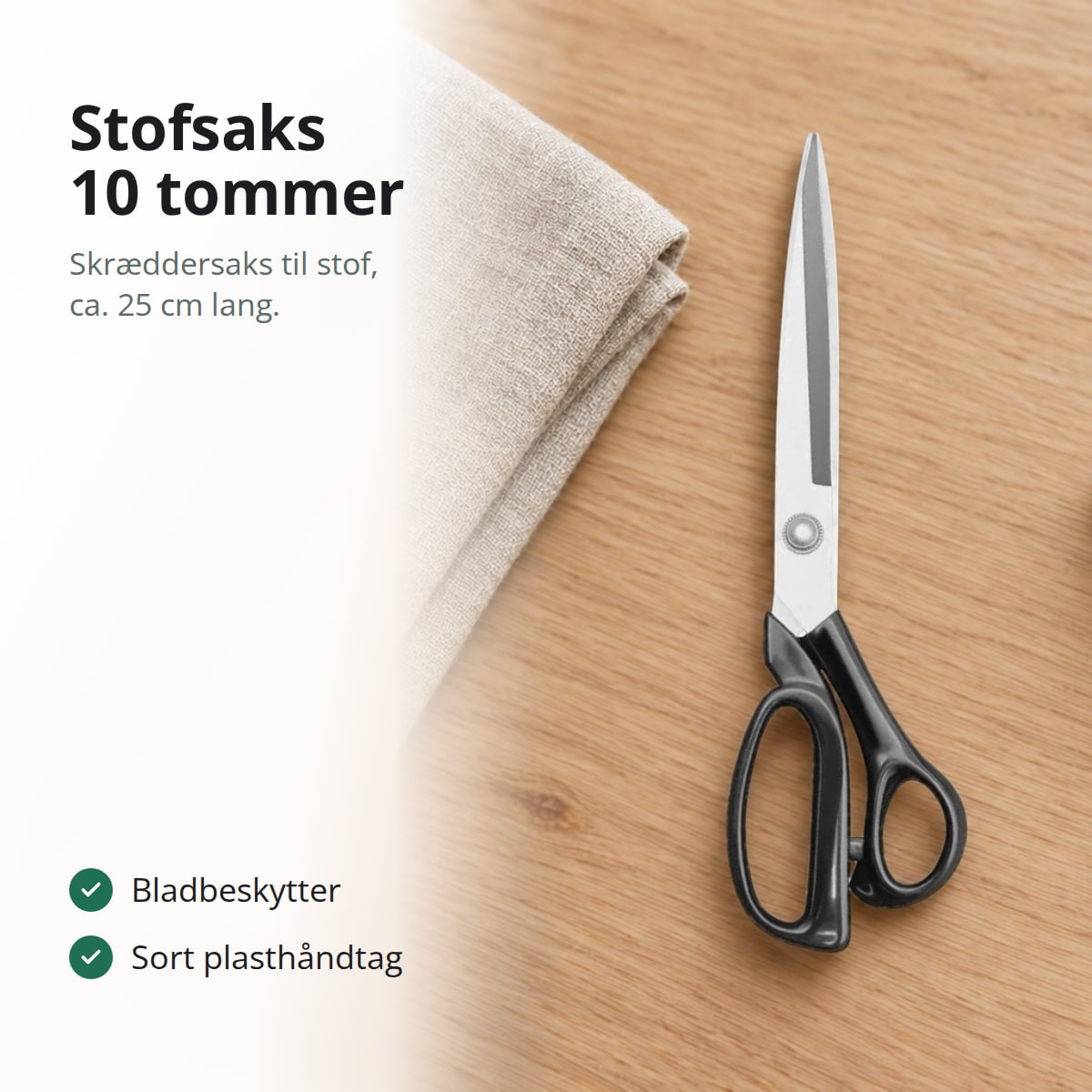 Stofsaks med lange blade og sort håndtag på et træbord ved siden af hørstof, med teksten: stofsaks 10 tommer, skræddersaks til stof, ca. 25 cm lang, bladbeskytter, sort plasthåndtag