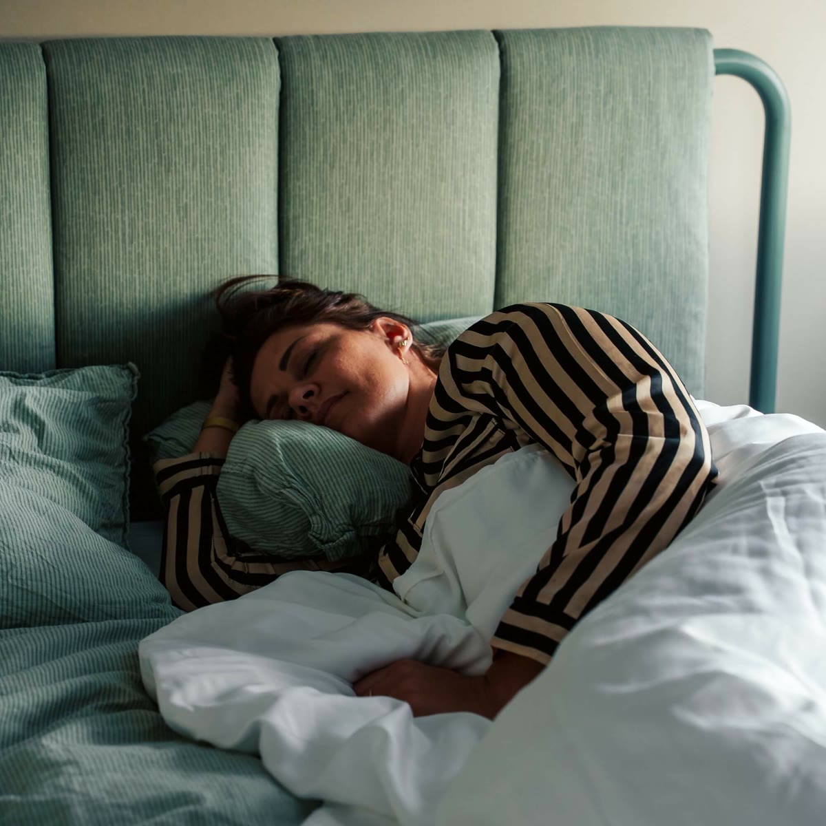Kvinde sover på siden under den hvide tyngdedyne i en seng med grøn gavl