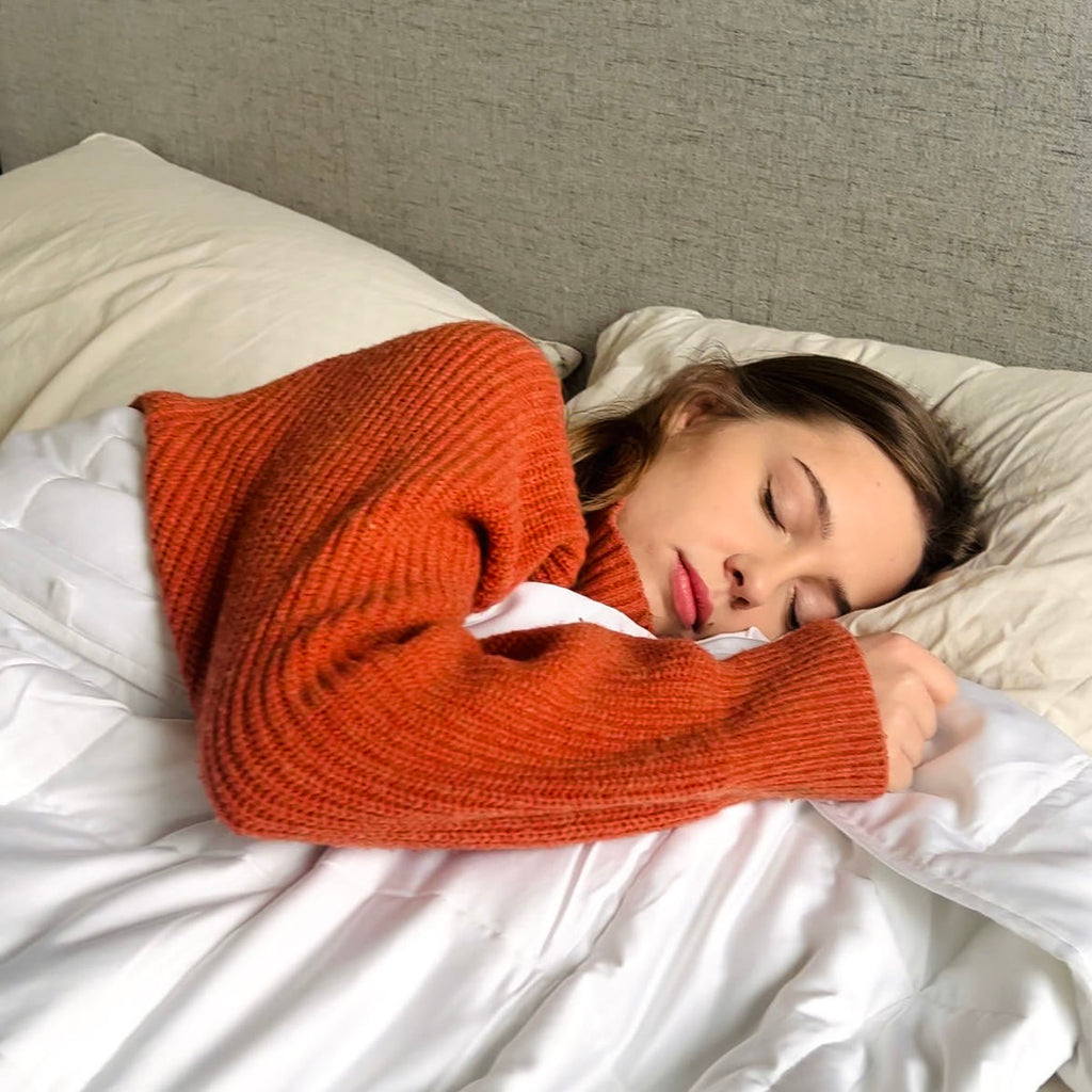 Kvinde i orange sweater sover med tyngdedynen trukket op til hagen