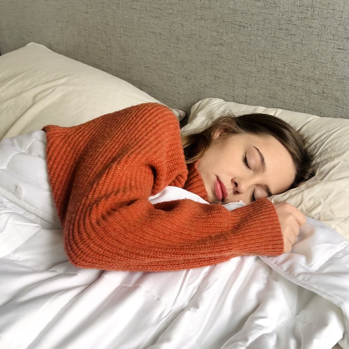 Kvinde i orange sweater sover med tyngdedynen trukket op til hagen