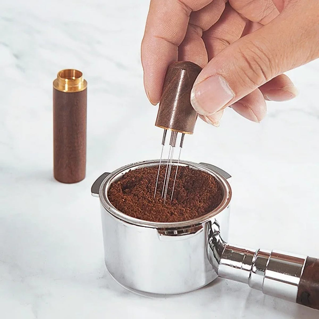 Hånd, der rører med WDT-værktøjet i den malede kaffe i en filterkurv, med låget ved siden af